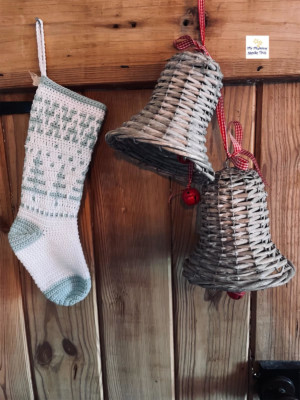 Pale blue and white christmas stocking hanging next to wicker Christmas bells